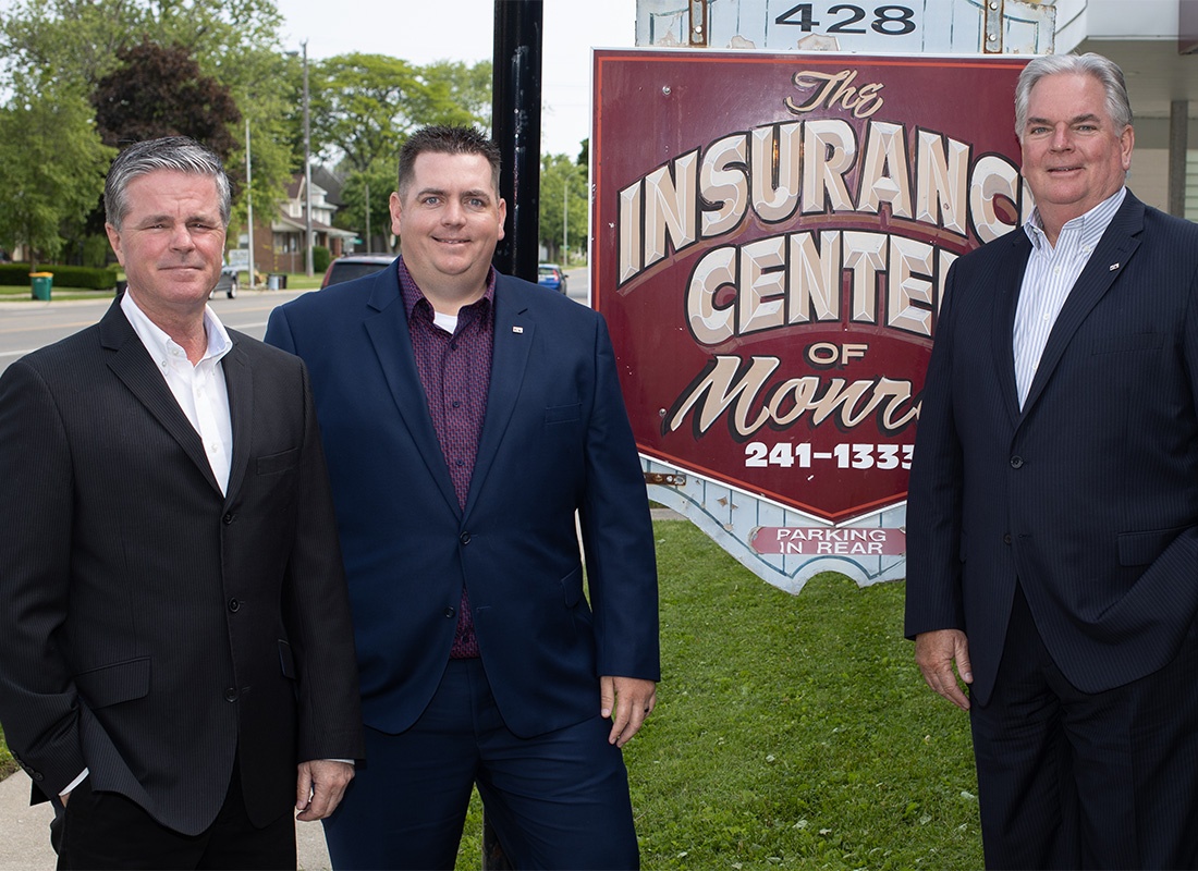 About Our Agency - Portrait of Three Insurance of Monroe Center Agents Wearing Business Suits Standing Outside the Office Building in Front of the Agency Sign